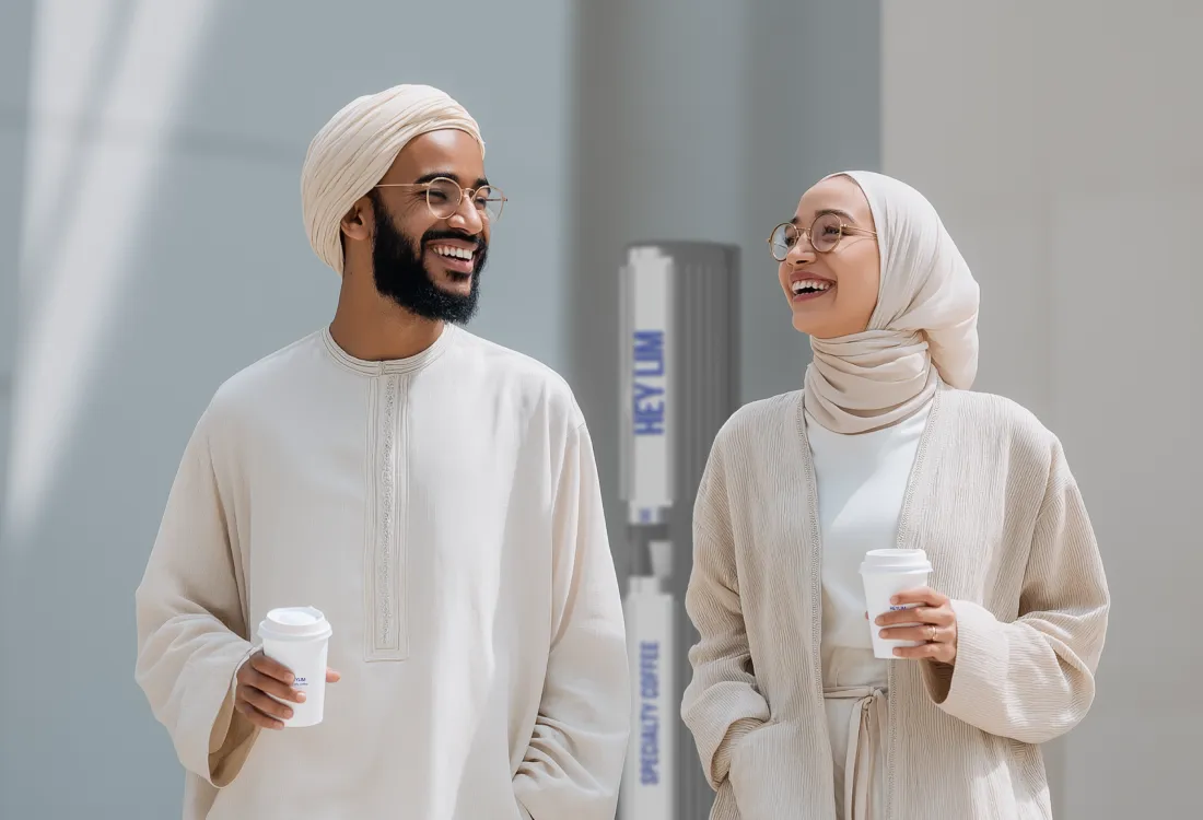 زوجان إماراتيان يحملان أكواب قهوة من مقهى HEYLIM الذاتي — حيث يلتقي الزيّ التقليدي بثقافة القهوة المعاصرة